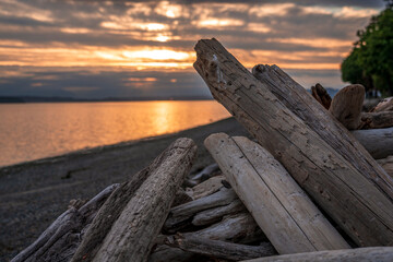 Driftwood logs are piled up on a Pacific Northwest beach as the sun sets over the Olympic Mountains in Washington State, USA.