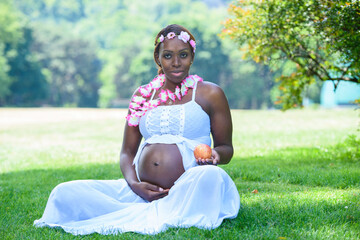 Pregnant Afro mom is sitting in nature shows off her baby bump while holding an apple. Health and...