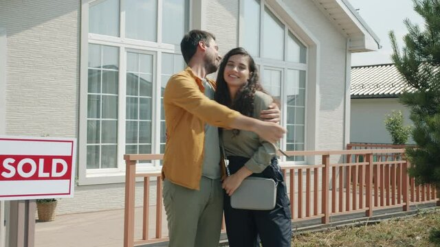 Portrait of man and woman new house owners standing outdoors holding keys hugging smiling enjoying property purchase. Youth and accommodation concept.