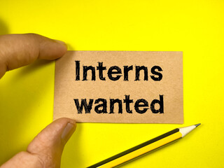 Business concept.Text Interns wanted on brown card with hand and pencil on a yellow background.