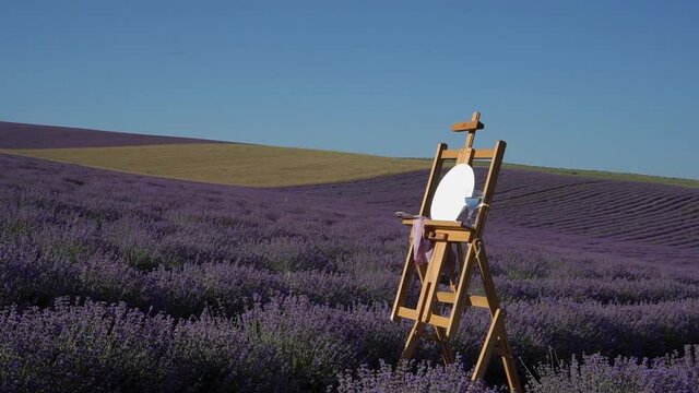 An artist's easel with a round canvas palette of paints and brushes. Plein air in nature. View of the lavender and wheat field. Landscape in Provence France