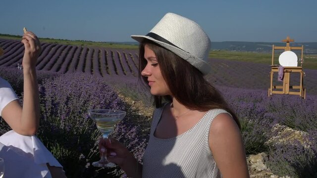 Beautiful girl in a hat with a glass of wine. Outdoor art picnic at the lavender field. Romantic plein air scene on summer day. Open-air party. Rustic landscape. Provence France Europe