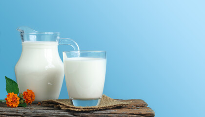 A jug of milk and glass of milk on a wooden table on a blue background.