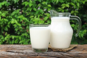 A jug of milk and glass of milk on a wooden table.