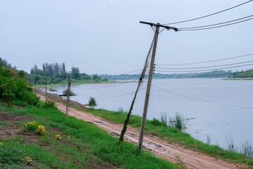 An old electric pole is on the edge of a rural dirt road. This road is on the edge of a large pond.