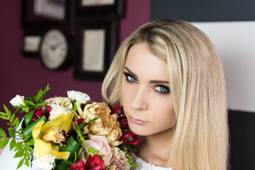 Portrait of a beautiful blonde girl with a box of flowers stands in the purple room with a retro style. Close up