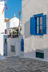 Traditional cycladitic   alley with a narrow street, a whitewashed  church and  blooming flowers in...