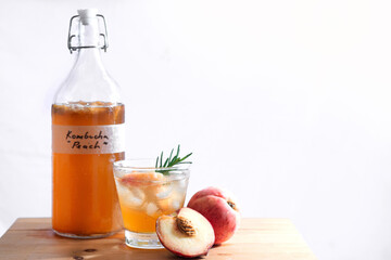 Homemade fermented raw Kombucha tea, healthy natural probiotic flavored drink, bottle and glass of Kombucha drink on wooden background with peach, white background