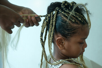 Close up African hairstylist braided hair of afro little girl, mother spend time with girl child take care and relaxing at home together, selective focus