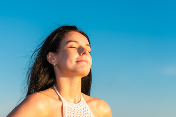 Beautiful girl breathing and smiling on the beach with the blue sky in the background.