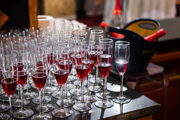a pile of pink champagne glasses, some full, and an ice bucket with bottles in the back, ready to be served to guests at an event. waiter