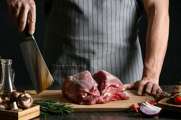Man with raw pork meat and vegetables on dark table