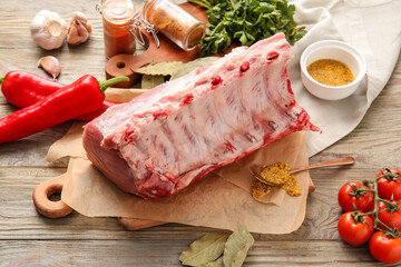 Parchment with raw pork ribs, spices and vegetables on wooden background, closeup