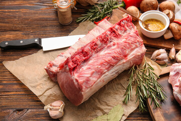 Parchment with raw pork ribs and spices on wooden background