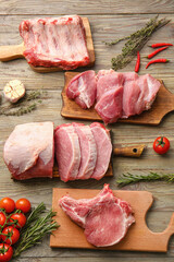 Boards with slices of raw pork meat, tomato and garlic on wooden background