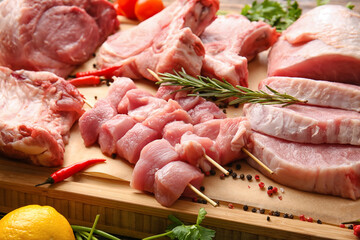 Slices of raw pork meat and spices on wooden board, closeup
