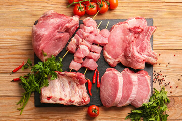 Slate plate with slices of raw pork meat, spices and tomato on wooden background
