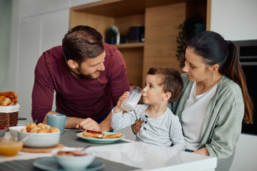 Young happy parents enjoy in breakfast with their little son at home.