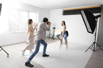 Photographer taking picture of stylish young woman in studio