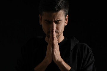 Religious young man praying on dark background