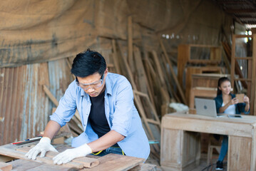 Serious Asian male carpenter in goggles and gloves, putting and holding the pieces of woods...