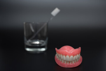 Full removable plastic denture of the jaws. Two acrylic dentures. Dental care with an toothbrush. Teeth and toothbrush on a dark background. Dental prosthesis care. Oral hygiene. Copy space