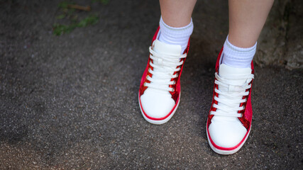 Photo of female legs in red and white sneakers on gray wet asphalt. Red and white sneakers with white laces close up