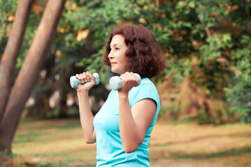 Middle aged elderly active woman doing exercise with dumbbells in a park outdoor