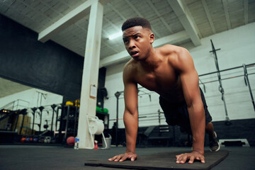 Young African American male doing push-ups in the gym. Mixed race, male personal trainer doing...