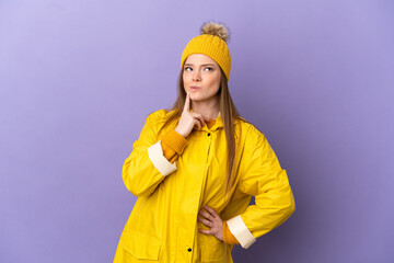 Teenager girl wearing a rainproof coat over isolated purple background having doubts while looking up