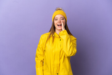 Teenager girl wearing a rainproof coat over isolated purple background shouting with mouth wide open