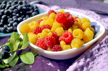 Photo of raspberries and blueberries illuminated by the sun. Delicious yellow and red raspberries on a small saucer. Yellow raspberries.
