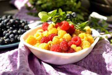 Photo of raspberries and blueberries illuminated by the sun. Delicious yellow and red raspberries on a small saucer. Yellow raspberries.
