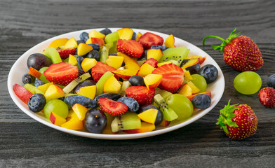 Salad in a white plate made of fresh fruits from grapes, nectarine, kiwi and strawberries, blueberries, honeysuckle on a dark wooden background.Top view, copy of the space
Категория
Еда
