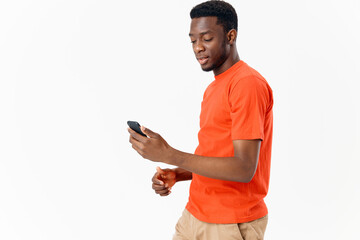 handsome african man with mobile phone on light background and orange t-shirt shorts