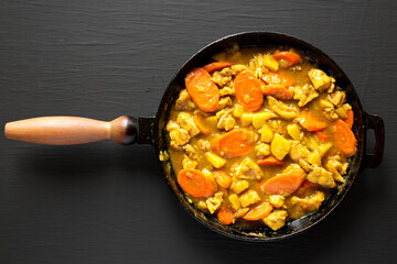Homemade Japanese Chicken Curry in a cast-iron pan on a black background, top view. Flat lay, overhead, from above.