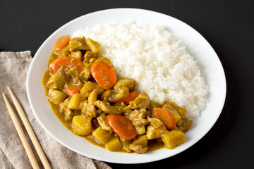 Homemade Japanese Chicken Curry  on a white plate on a black surface, side view.
