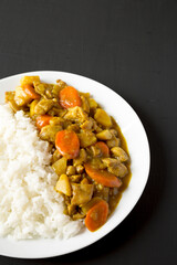 Homemade Japanese Chicken Curry  on a white plate on a black background, side view. Copy space.