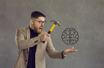 Crazy angry man in suit and glasses holding hammer over brain doodle isolated on grey background. Guy experiencing mental disorder, stress, problems, or lack of creativity hitting brain and screaming