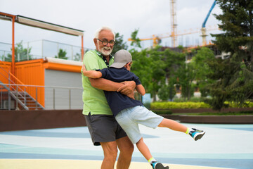 A little boy is enjoying the playground with Grandfather. Grandpa is lifting him and spinning.