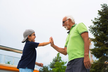 A happy little boy and his grandfather are throwing a high five at each other.