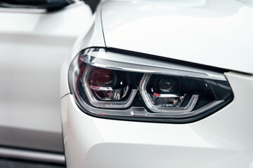 Fototapeta premium Front headlight of a white luxury modern suv car close up.