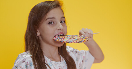 Happy child sucking lollipop on yellow background