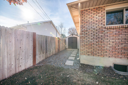 Side yard of a house with vinyl shed against a wooden fence