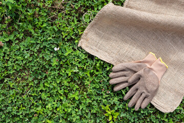 Farming or gardening flat lay background with copy space. Garden gloves and sackloth bag on the green grass top view background.