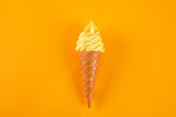 Top view of yellow ice cream on a cone isolated on an orange background