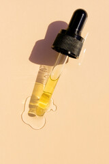 close up of pipette with pouring liquid serum and shadows on beige background. Trendy cosmetics...