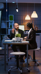 Multi-ethnic businesspeople working overtime in office meeting room discussing management graphs planning company strategy late at night. Divers teamwork brainstorming financial presentation ideas
