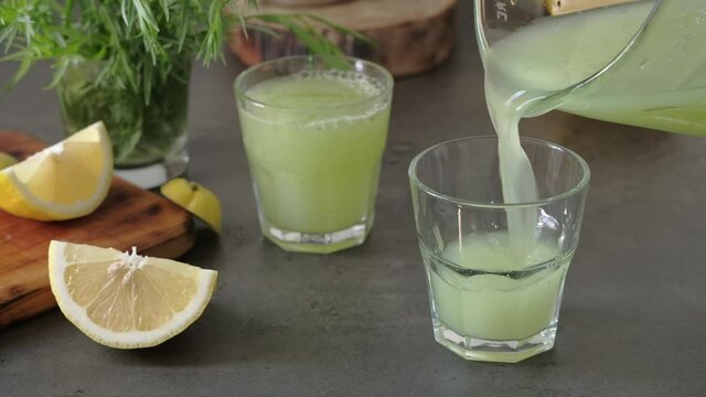 Healthy lemonade with ice and tarragon for detoxification is poured into glasses. Cold non-alcoholic summer drink. Cooling drink preparation concept. Real time 4 k video