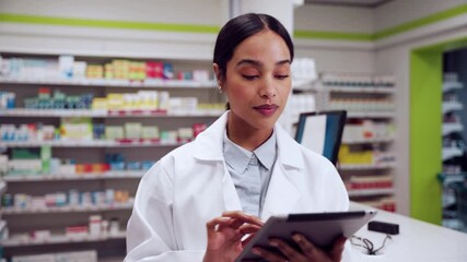 Mixed race female pharmacist working in clinic checking dates on medicines using digital tablet